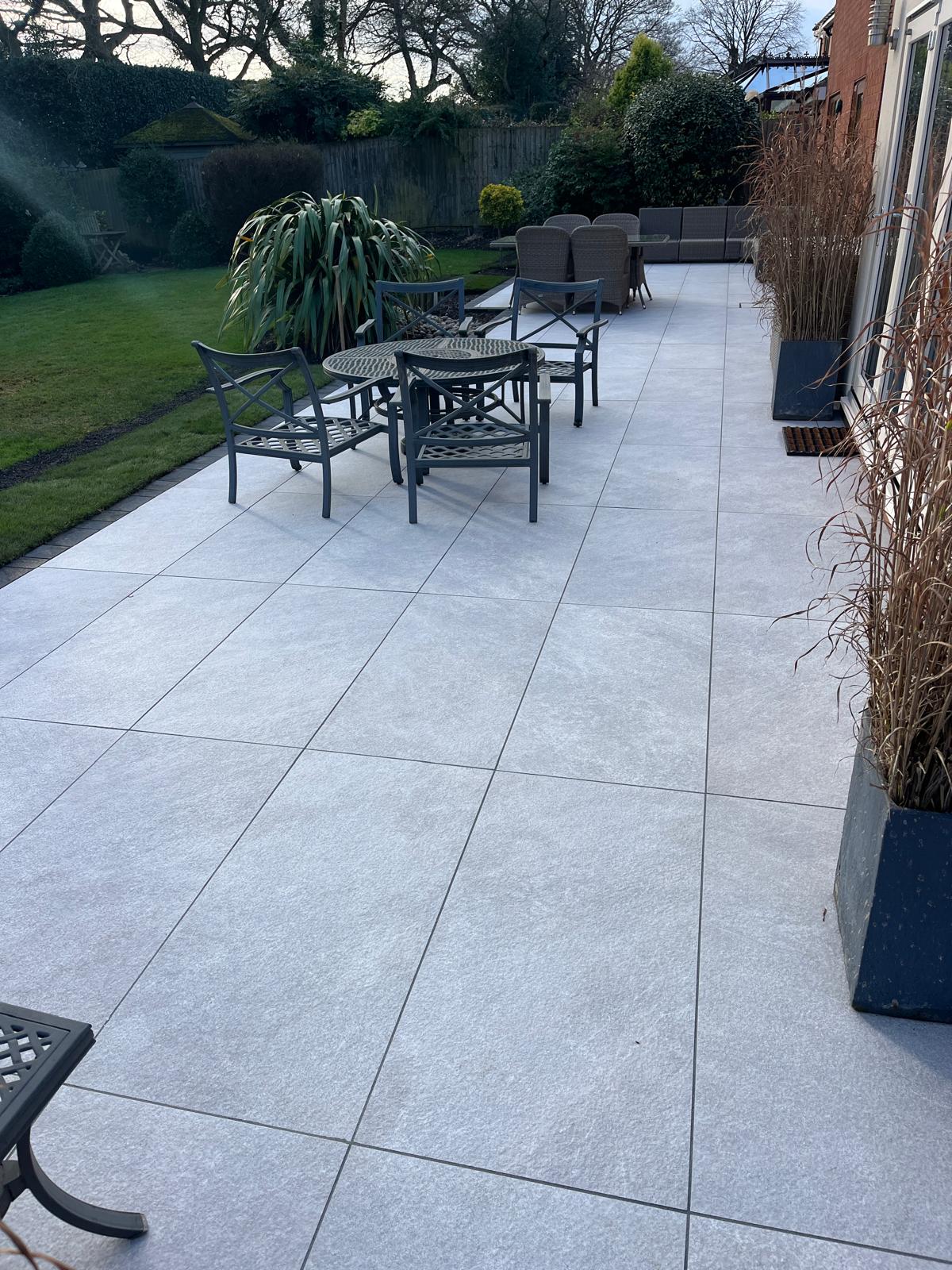 Completed pale stone patio with outdoor dining space alongside a brick home